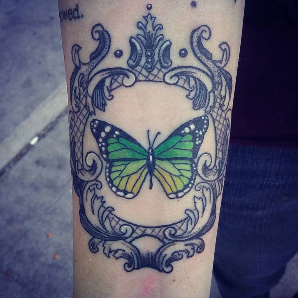 Green and yellow butterfly tattoo framed by black ornamental scrollwork on the forearm by Danae at Broken Clover Tattoo in Tucson