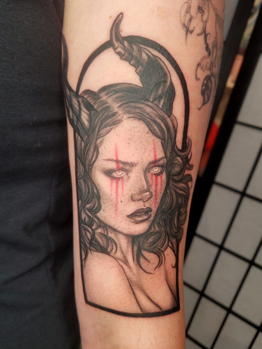 Black-and-grey dark fantasy tiefling woman tattoo with red eye makeup by Jasmine at Broken Clover Tattoo in Tucson