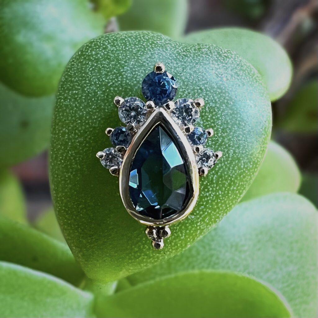 A teardrop London blue topaz set in gold with small CZ accent stones displayed on a succulent leaf.