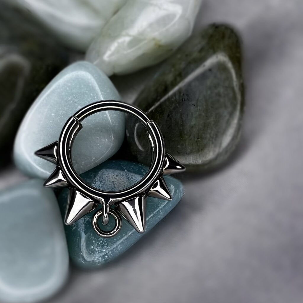 Titanium spiked collar clicker ring displayed on polished blue and green stones.