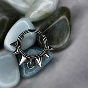 Titanium spiked collar clicker ring displayed on polished blue and green stones.