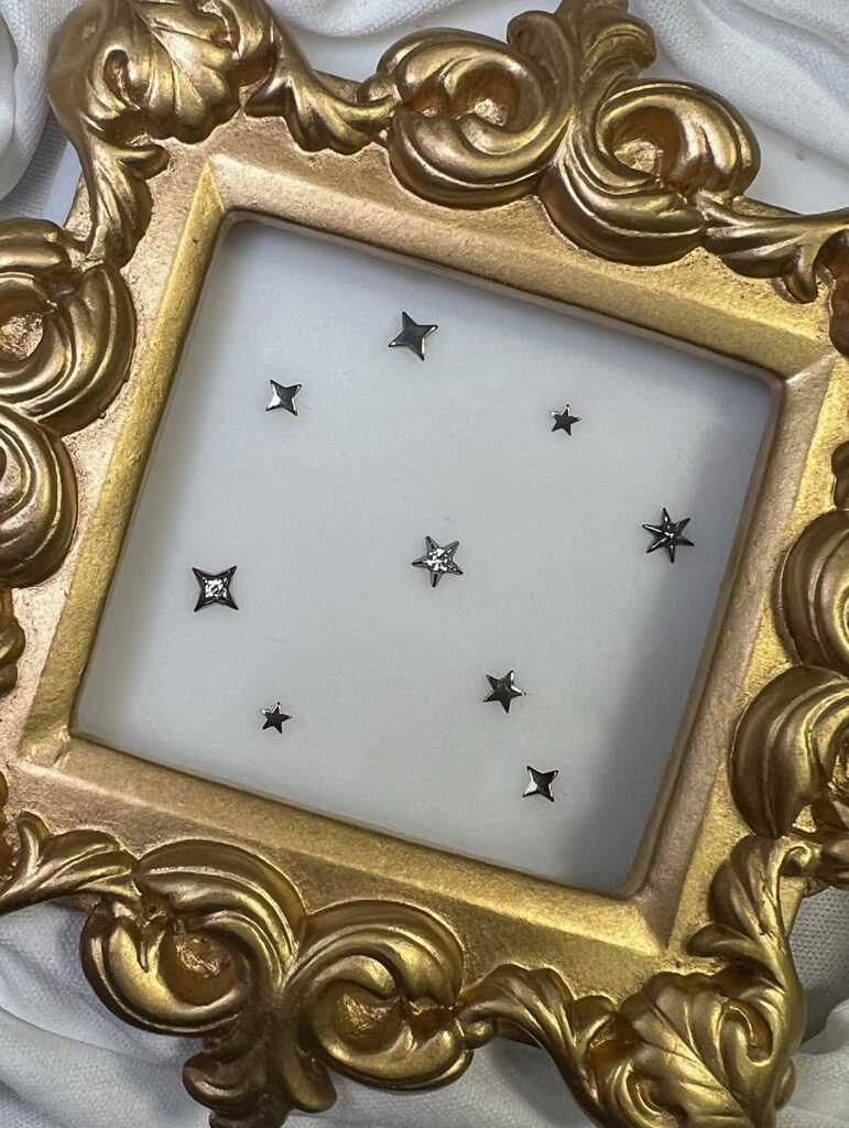 Titanium threadless star‑shaped ends with gemstone accents displayed inside an ornate gold frame.