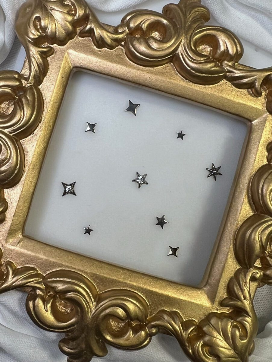 Titanium threadless star‑shaped ends with gemstone accents displayed inside an ornate gold frame.