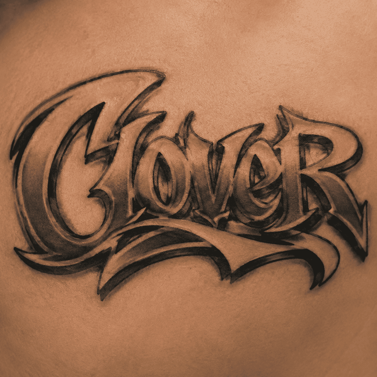 Bold black-and-gray graffiti-style tattoo spelling “Clover,” representing the Graffiti / street letters choice in Question 8 of the Broken Clover artist quiz.