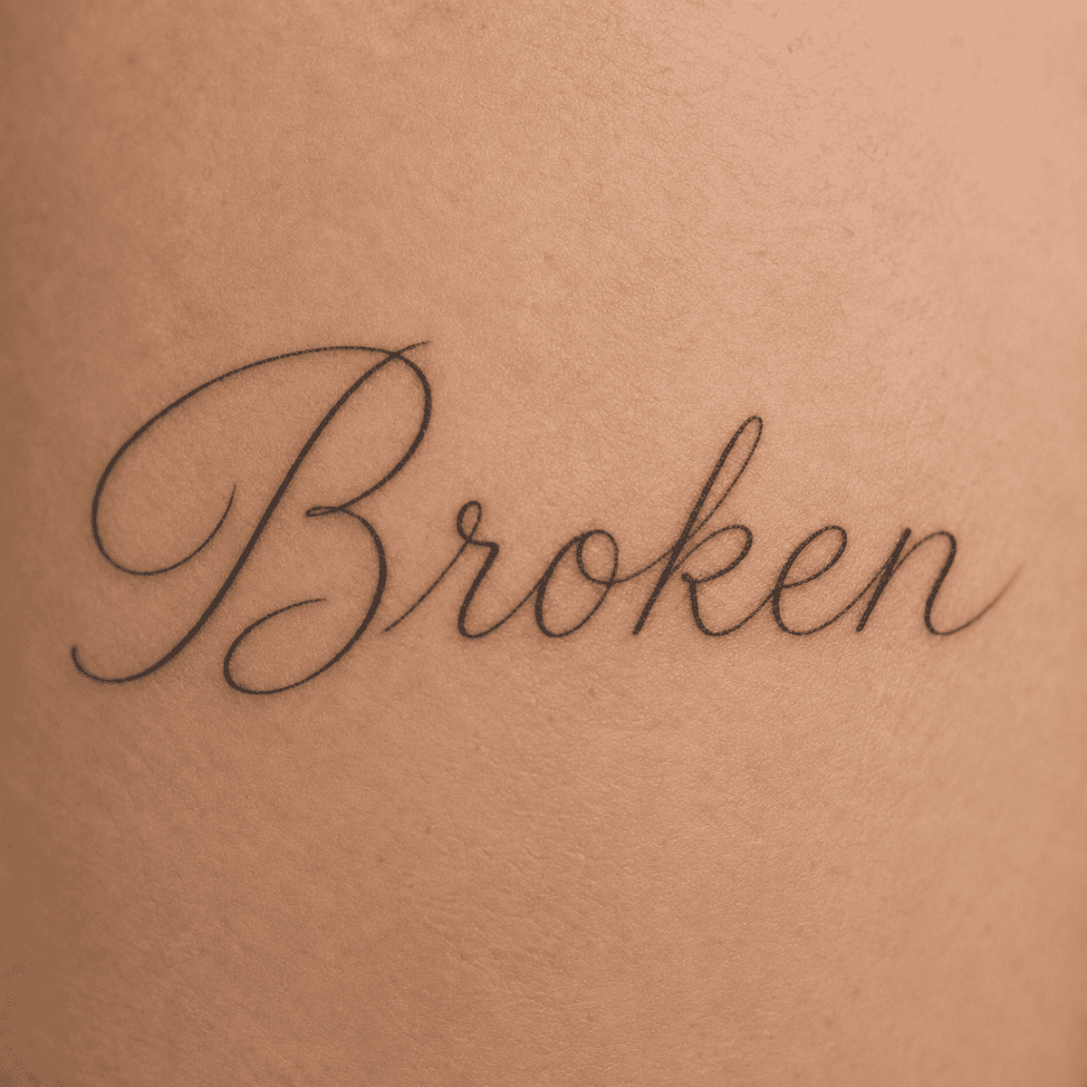 Delicate fine-line script tattoo spelling “Broken,” representing the Thin script / clean lettering choice in Question 8 of the Broken Clover artist quiz.